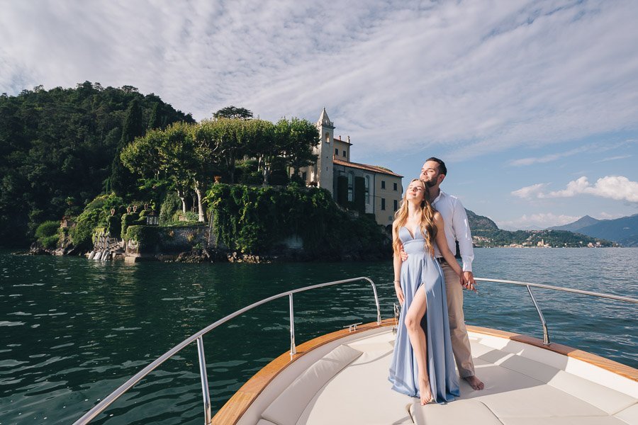 A Young Couple Poses In Front Of Villa Del Balbianello standing on the boat