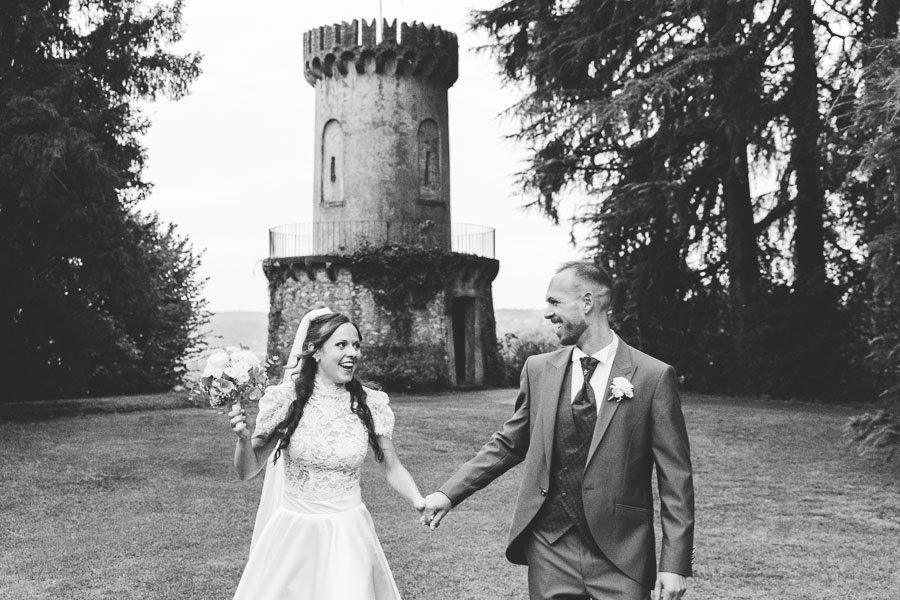 Newlyweds Walks Happily In Garden under a tower