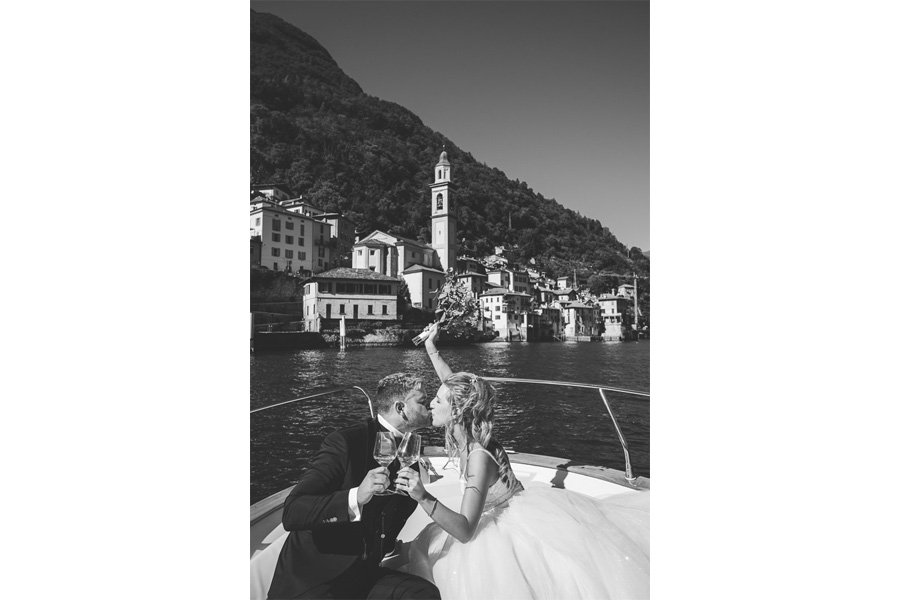 Two Happy Newlyweds Kiss While Toasting In Front Of The Church Of Brienno
