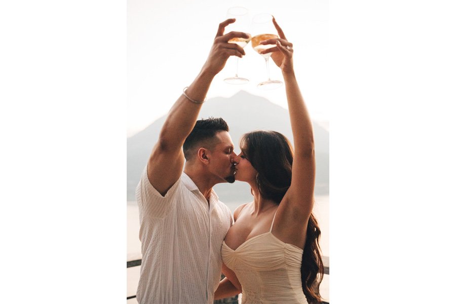 Two New Fiancés Kiss While Raising Their Glasses At Sunset in lake como